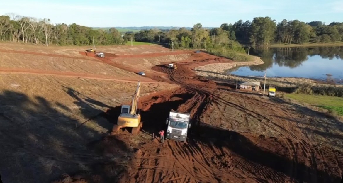 Escavadeira e caminhão trabalhando na margem do lago dentro da área do condomínio